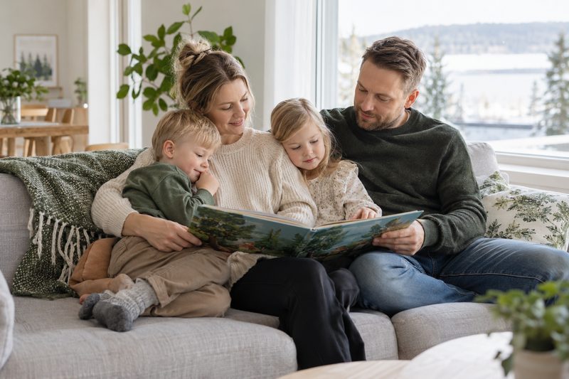Vanhemmat ja kaksi lasta lukevat kuvakirjaa yhdessä sohvalla